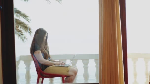 Estudante bonita ou freelancer trabalhando em um laptop, mulher sentada na varanda com vista superior palma e mar, vídeo rápido, câmera lenta, hd completo — Vídeo de Stock
