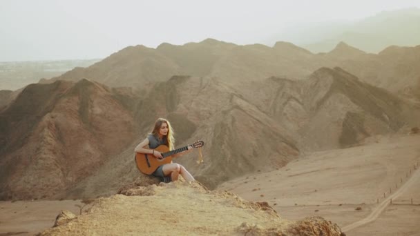 Mulher tocando guitarra e cantando em paisagens desérticas, deserto montanhas fundo, câmera lenta, hd completo — Vídeo de Stock