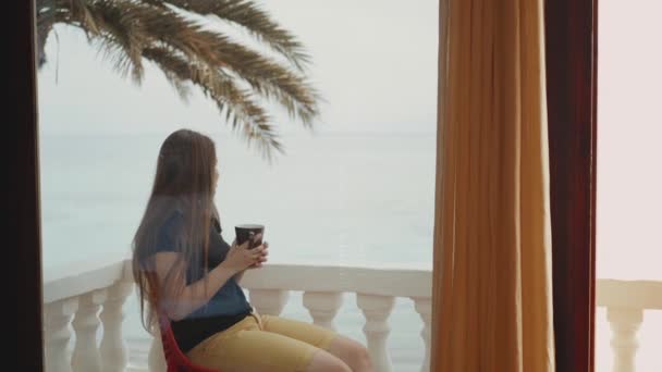 Donna sola sta bevendo caffè o tè al mattino sul balcone con vista mare blu, punto di vista dalla finestra, video rapido, rallentatore, full hd — Video Stock