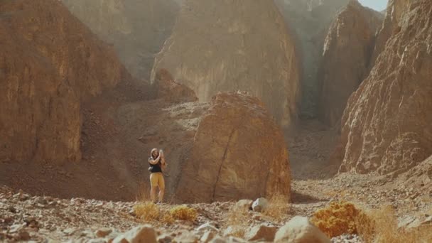 Mulher turística caminhar ao longo do cânion de rocha e tirar fotos no deserto quente. Desert canyon fundo, Egito, Sinai, câmera lenta, Full hd — Vídeo de Stock