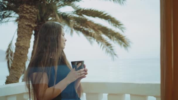 Μόνος γυναίκα πίνει καφέ ή τσάι το πρωί στο μπαλκόνι με μπλε θέα στη θάλασσα, άποψη από το παράθυρο, γρήγορη βίντεο, αργή κίνηση, full hd — Αρχείο Βίντεο