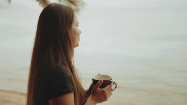 Sama žena pije kávu nebo čaj v dopoledních hodinách na balkóně s modrým výhledem na moře, pohled z okna, rychlé video, zpomalení, full hd — Stock video