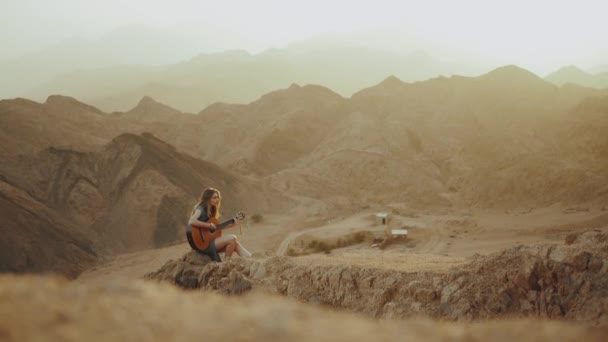 Wanita bermain gitar dan bernyanyi di padang pasir, padang pasir pegunungan latar belakang, gerakan lambat, hd penuh — Stok Video