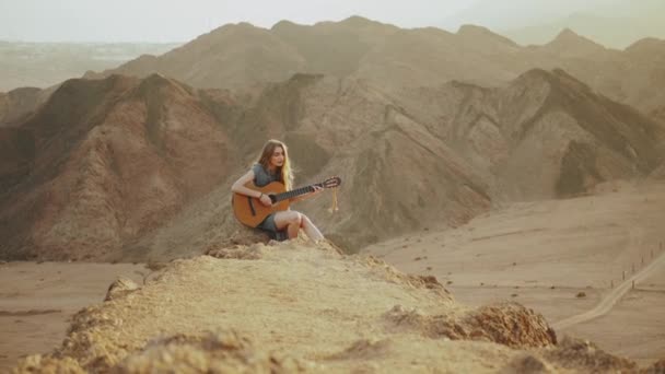 Woman playing guitar and singing in desert landscapes, desert mountains background, slow motion, full hd — Stock Video