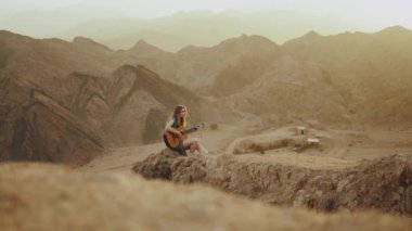 Gitar çalan ve çöl manzaralarında şarkı söyleyen kadın, çöl arkası, yavaş çekim, tam hd