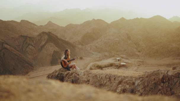 Mulher tocando guitarra e cantando em paisagens desérticas, deserto montanhas fundo, câmera lenta, hd completo — Vídeo de Stock