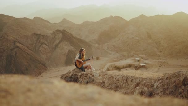 Женщина играет на гитаре и поет в пустынных пейзажах, пустынные горы фон, замедленное движение, полный hd — стоковое видео