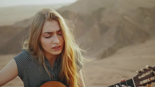 Kobieta gra na gitarze i śpiewa w pustynnych krajobrazach, pustynne tło gór, zwolnione tempo, pełny hd — Wideo stockowe
