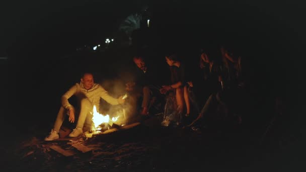 Bir grup arkadaş, gece deniz kenarındaki kumsalda kamp ateşinin yanında eğleniyor. Hızlı video, yavaş çekim, tam yol ileri. — Stok video