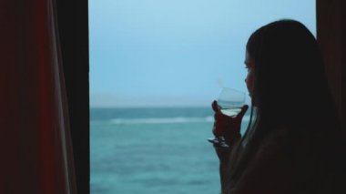 Kadın şarap içiyor ve bak insanlar Dahab Mısır 'da temiz suda nasıl sörf yapıyor. Arka planda dağlarla mavi denizi keşfetmek ve insanlar uçurtma sörfü, yavaş çekim, tam yol ileri.