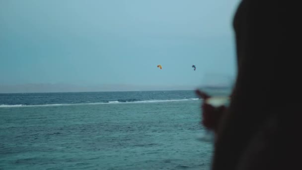 Γυναίκα πίνουν κρασί και να δούμε πώς οι άνθρωποι Kite surfing σε όμορφα καθαρά νερά στην Dahab Αίγυπτο. Εξερευνώντας τη γαλάζια θάλασσα με τα βουνά στο παρασκήνιο και οι άνθρωποι kite surfing, αργή κίνηση, full hd — Αρχείο Βίντεο