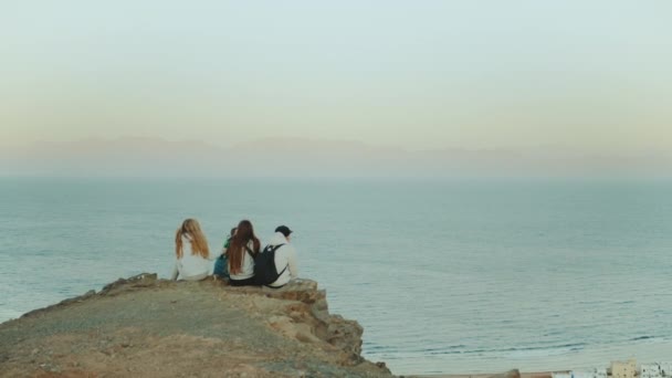 Grupo de amigos relajándose en la cima de una montaña al atardecer y disfrutando de la vista al mar - amistad, juventud, cámara lenta, full hd — Vídeos de Stock