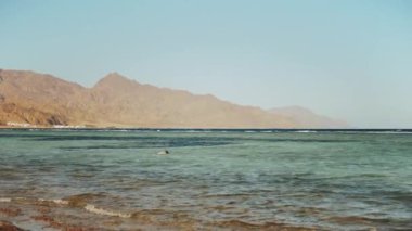 Kızıl denizde şnorkelle yüzen adam, güzel mavi deniz manzarası ve berrak gökyüzü, denizdeki dalgalar ve ufuktaki dağlar, Mısır, Dahab, yavaş çekim, tam hd