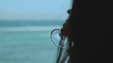 Kadın şarap içiyor ve bak insanlar Dahab Mısır 'da temiz suda nasıl sörf yapıyor. Arka planda dağlarla mavi denizi keşfetmek ve insanlar uçurtma sörfü, yavaş çekim, tam yol ileri.