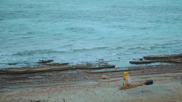 Mujer bonita sentada sola en la playa costera pedregosa cerca del mar, las olas se rompen en la orilla, Egipto Sinaí montaña en el fondo, cámara lenta, hd completo — Vídeos de Stock