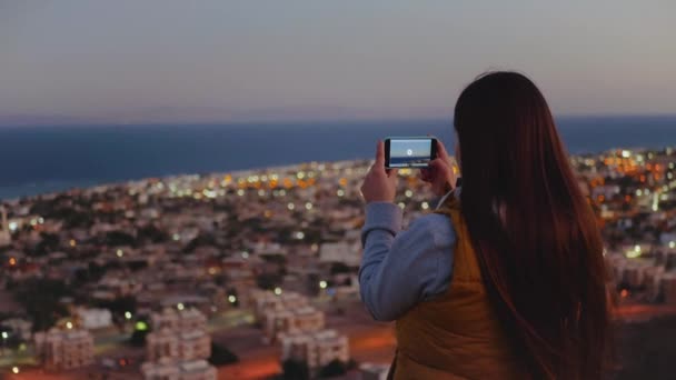 Mujer tomar una foto del mar por teléfono inteligente en la noche. Mujer permanecer en la cima de la montaña y mirando en Horizonte, cámara lenta, full hd — Vídeo de stock