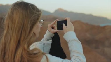 Sarışın kadın akıllı telefondan denizin fotoğrafını çekiyor. Kadın dağın tepesinde durur ve Horizon 'a bakar, ağır çekimde, tam yol ileri.