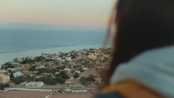 Widok na błękitne morze i małą wioskę z tyłu kobiety. Dziewczyna pozostać na szczycie góry i patrząc w Horyzont, zwolnione tempo, pełne hd — Wideo stockowe