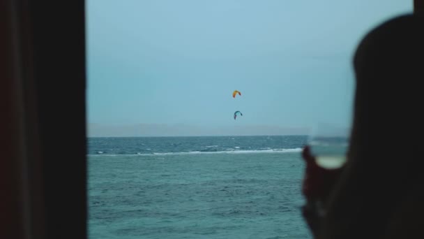 Mulher beber vinho e veja como as pessoas Kite surf em água limpa bonita em Dahab Egito. Explorando o mar azul com montanhas no fundo e as pessoas kite surf, câmera lenta, hd completo — Vídeo de Stock