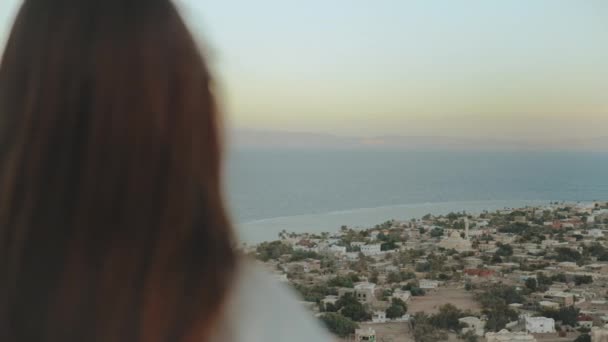 Vue de la mer bleue et petit village de dos de femme. Fille rester au sommet de la montagne et regarder dans l'horizon, ralenti, full hd — Video