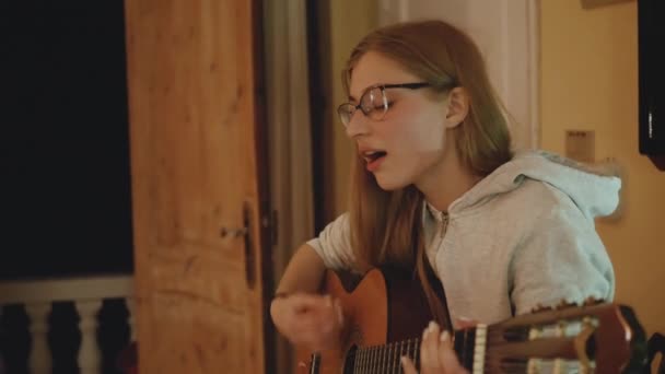 안경을 쓴 금발의 여자가 기타를 연주하고 아늑 한 아파트 의자에서 노래를 부른다. 여자 가 실내에서 느린 동작으로 음악을 만지작 거린다 — 비디오
