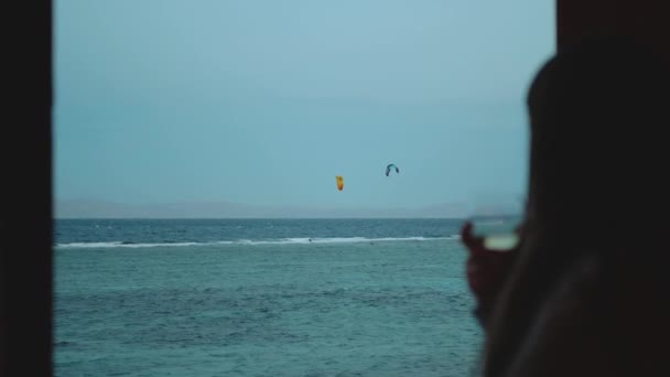 Femme boire du vin et regarder comment les gens cerf-volant surf dans une belle eau claire à Dahab Egypte. Explorer la mer bleue avec des montagnes en arrière-plan et les gens kite surf, ralenti, full hd — Video