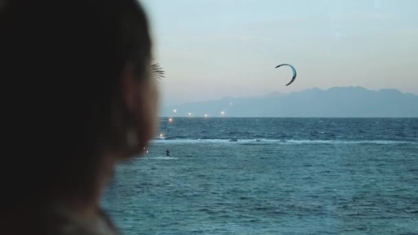 Femme boire du vin et regarder comment les gens cerf-volant surf dans une belle eau claire à Dahab Egypte. Explorer la mer bleue avec des montagnes en arrière-plan et les gens kite surf, ralenti, full hd — Video