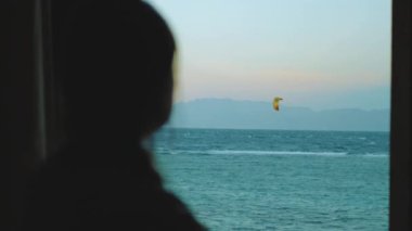Kadınlar, Dahab Mısır 'ın temiz sularında uçurtma sörfü yapan insanların güzelliğine bakar. Arka planda dağlarla mavi denizi keşfetmek ve insanlar uçurtma sörfü yapıyor, 4k