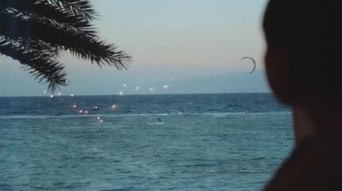 Kadınlar, Dahab Mısır 'ın temiz sularında uçurtma sörfü yapan insanların güzelliğine bakar. Arka planda dağlarla mavi denizi keşfetmek ve insanlar uçurtma sörfü yapıyor, 4k