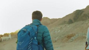 Bir grup turist sıcak çölde kaya kanyonu boyunca yürür, turistler fotoğraf çeker ve eğlenirler. Çöl Dağları, Mısır, Sina, 4k