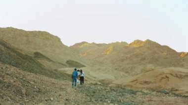 Bir grup turist sıcak çölde kaya kanyonu boyunca yürür, turistler fotoğraf çeker ve eğlenirler. Çöl Dağları, Mısır, Sina, 4k