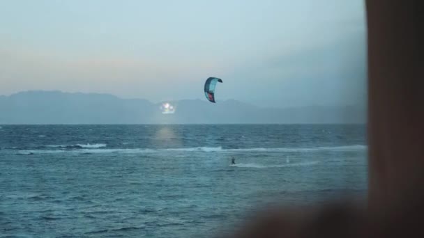 Kobieta pić wino i zobacz, jak ludzie kitesurfing w pięknej czystej wodzie w Dahab Egipt. Zwiedzanie błękitnego morza z górami w tle i ludzi kitesurfing, 4k — Wideo stockowe