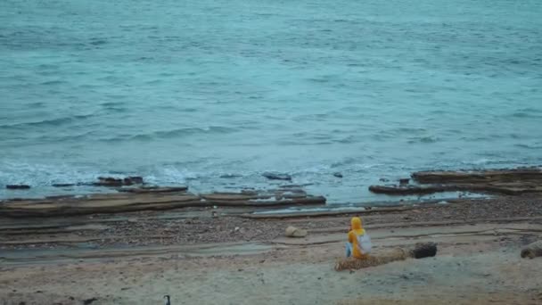 Hezká žena sedí sama na kamenité pobřeží pláže v blízkosti moře, vlny se lámou na břehu, Egypt Sinaj hora na pozadí, 4k — Stock video