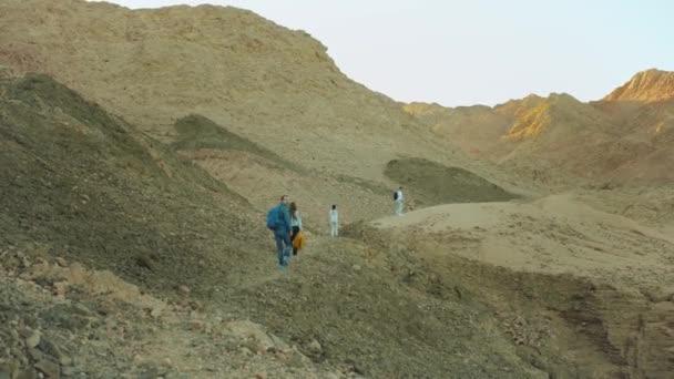 Grupo de paseo turístico a lo largo del cañón de roca en el desierto caliente, los turistas toman fotos y se divierten. Montañas del desierto de fondo, Egipto, Sinaí, 4k — Vídeo de stock