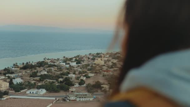 View of blue sea and small village from back of woman. Girl stay on top of the mountain and looking Into Horizon, 4k — Stock Video