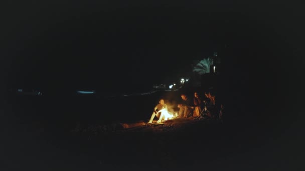 Grupo de amigos divirtiéndose cerca de la fogata en la playa cerca del mar por la noche, 4k — Vídeo de stock