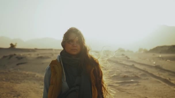 Портрет красивой женщины на закате в пустыне. Счастливая молодая женщина, стоящая на ветру на фоне закатного пейзажа пустыни Египет, 4k — стоковое видео