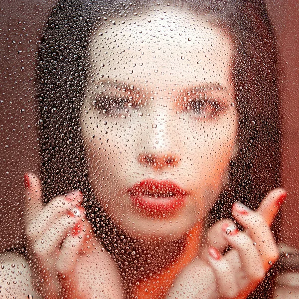 beautiful  woman face behind wet glass