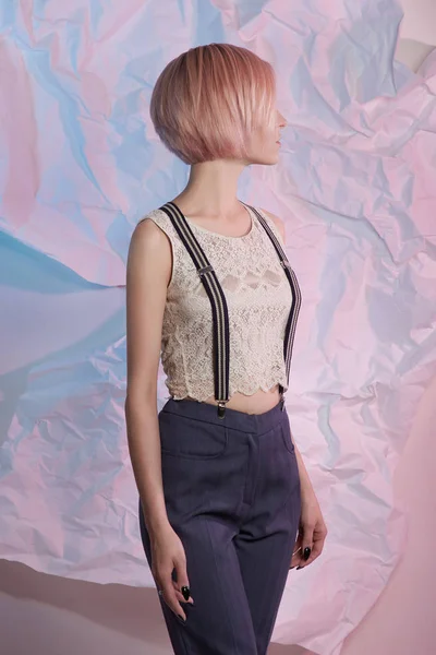 Young woman in pants with suspenders.blond bob hair model girl posing over color paper.business woman