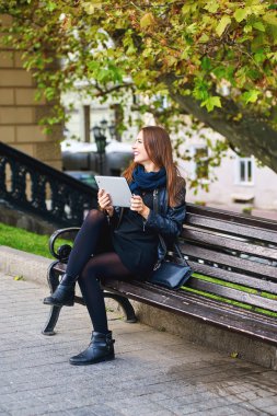 Eğlenceli kız bir şehirde Park oturan tablet aracılığıyla iletişim kurar
