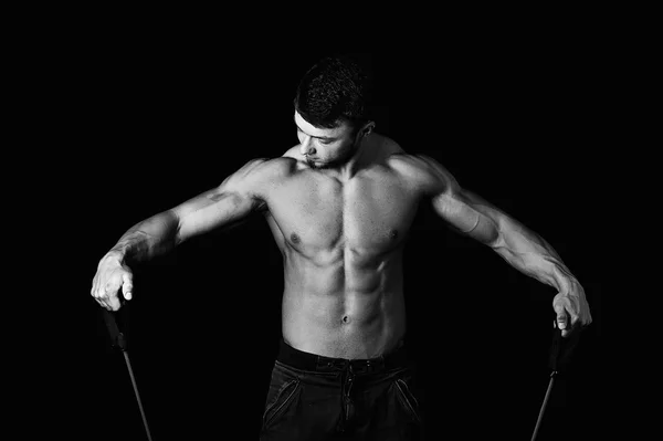 Homem jovem muscular está envolvido com o expansor .Estúdio em um fundo escuro, uma imagem em preto e branco — Fotografia de Stock