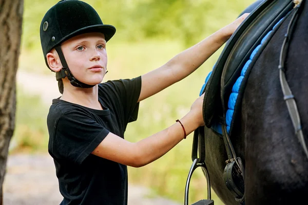男孩依然踏上征程的一匹马，并拧紧肚。训练马匹供人策骑 — 图库照片