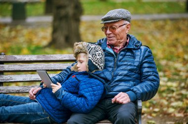 Torunu sonbahar Park ve bir tablet kullanarak okuma dedesi ile