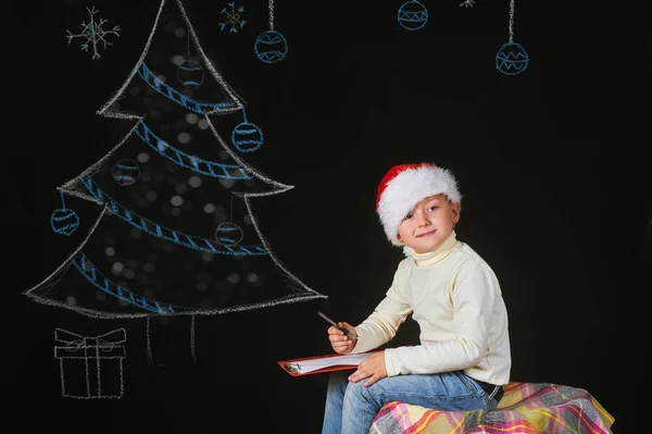 Retrato de niño hermoso en el sombrero de Santa Claus sobre un fondo oscuro, con árbol pintado — Foto de Stock