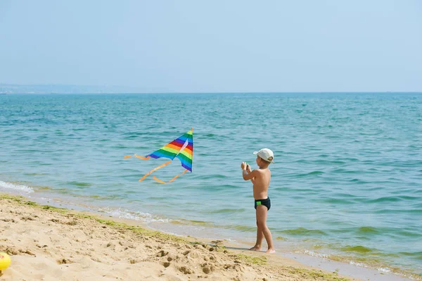 Kleiner Junge ruht sich aus und spielt am Strand mit einem Drachen — Stockfoto