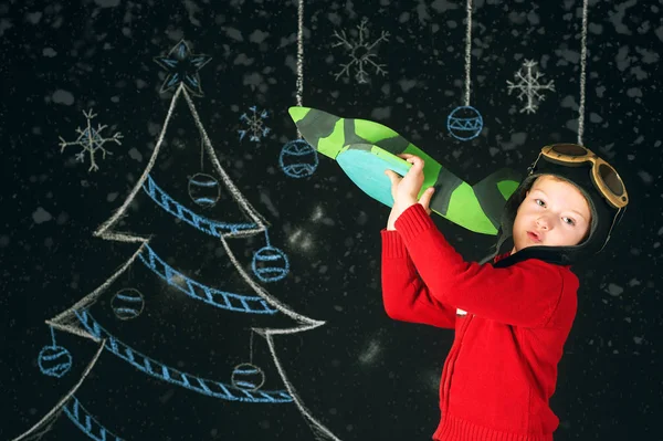 A handsome boy with a wooden toy plane , a retro helmet on a background with a painted tree — Stock Photo, Image