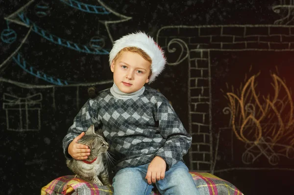 Jongen in KERSTMUTS poseren met een kat. Vrolijk kerstfeest — Stockfoto