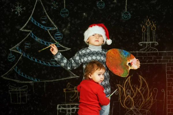 Brat i siostra na Boże Narodzenie tło, grając z paletą i pędzlami. Wesołych Świąt Bożego Narodzenia — Zdjęcie stockowe
