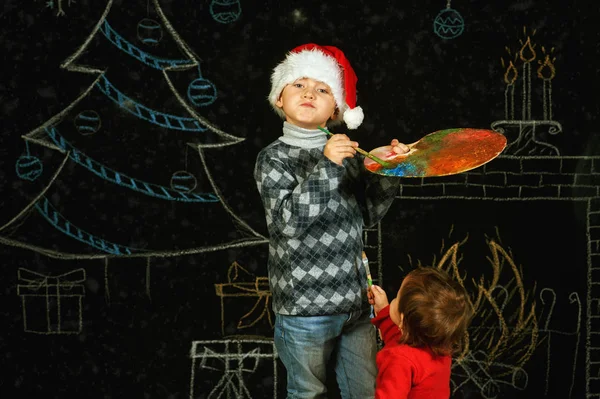 Brat i siostra na Boże Narodzenie tło, grając z paletą i pędzlami. Wesołych Świąt Bożego Narodzenia — Zdjęcie stockowe