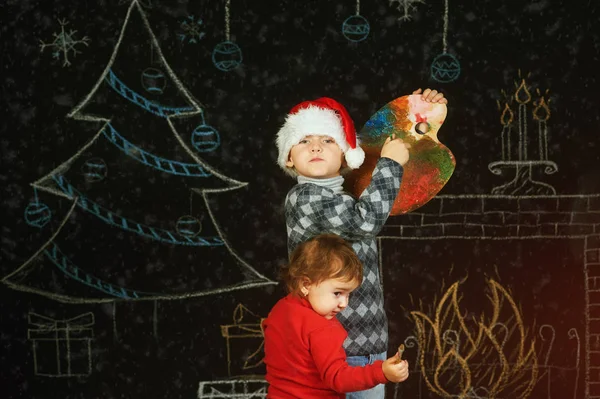 Irmão e irmã no fundo de Natal, brincando com uma paleta e pincéis.Feliz Natal — Fotografia de Stock